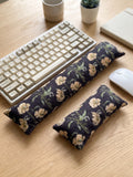 Black poppy corduroy keyboard and mouse wrist rests beside a keyboard on a wooden desk