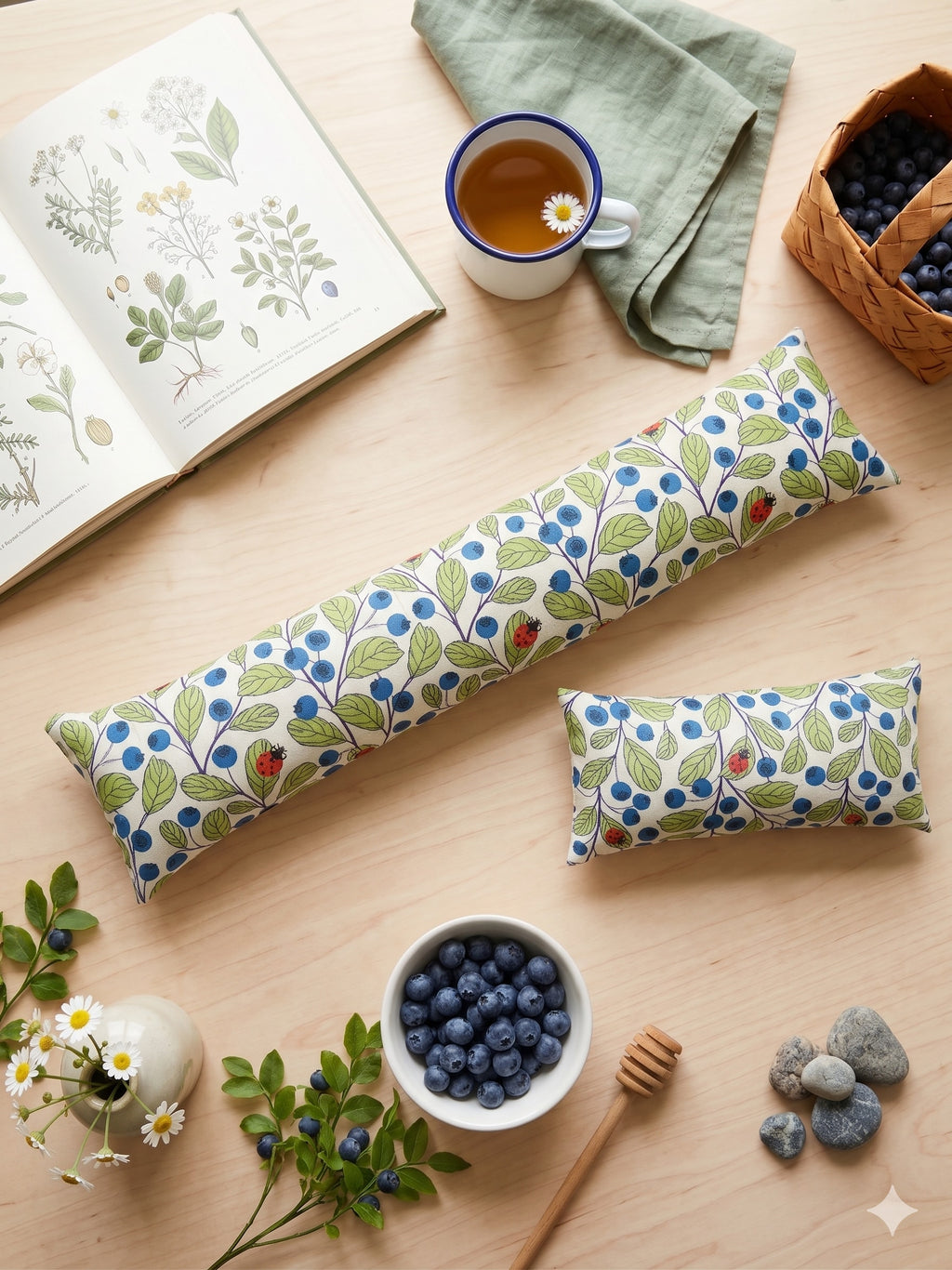The two pieces of the blueberry ladybug set among blueberries, tea and a botanical book