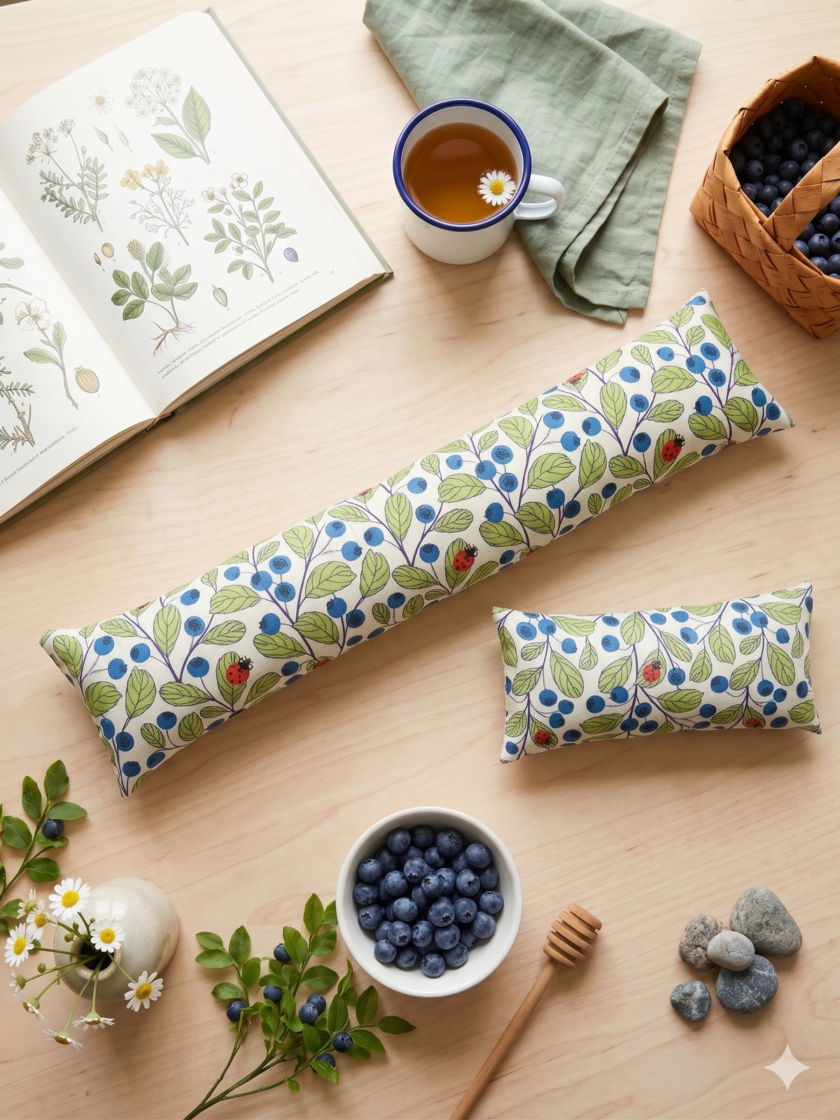 The two pieces of the blueberry ladybug set among blueberries, tea and a botanical book