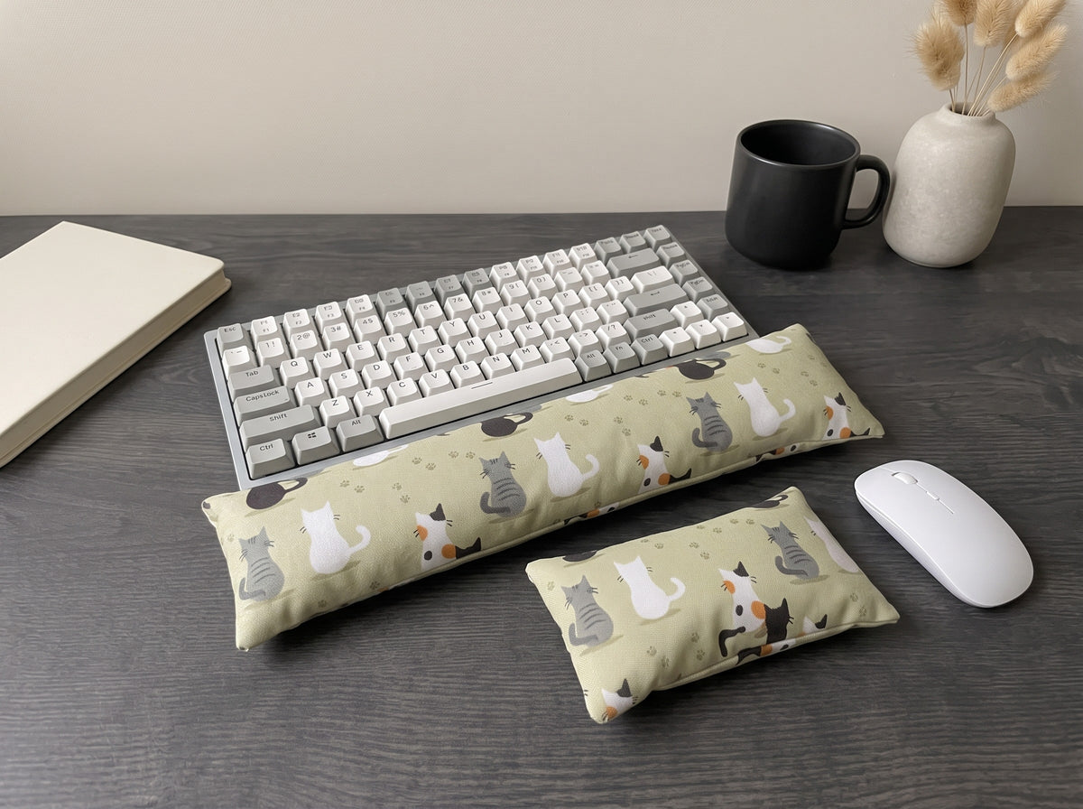 Calico cat family wrist rest set in front of a keyboard on a dark desk with a black mug