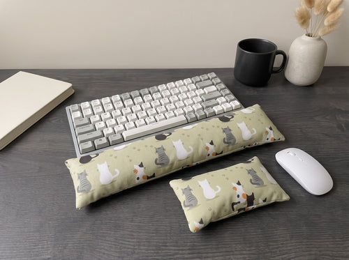 Calico cat family wrist rest set in front of a keyboard on a dark desk with a black mug