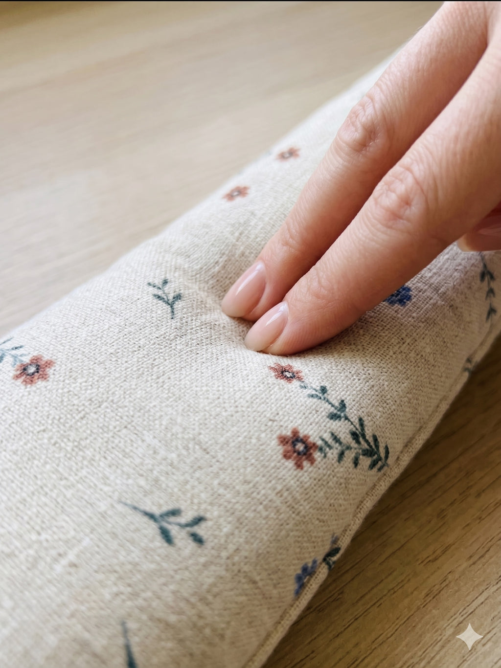 Hand pressing into the ditsy floral linen wrist rest to show the buckwheat filling