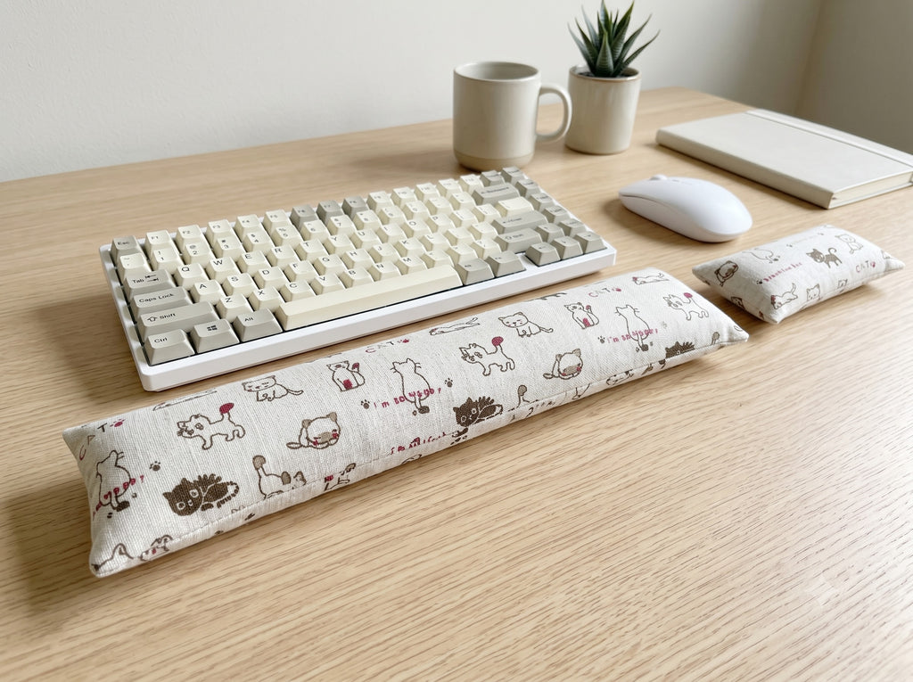 Natural doodle cat keyboard and mouse wrist rests in front of a keyboard on a wooden desk