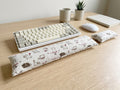 Natural doodle cat keyboard and mouse wrist rests in front of a keyboard on a wooden desk