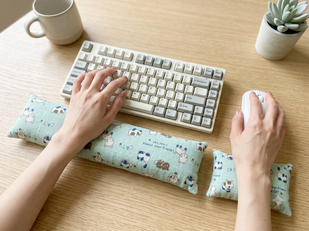 Hands on a keyboard and mouse resting on the mint doodle cat wrist rests