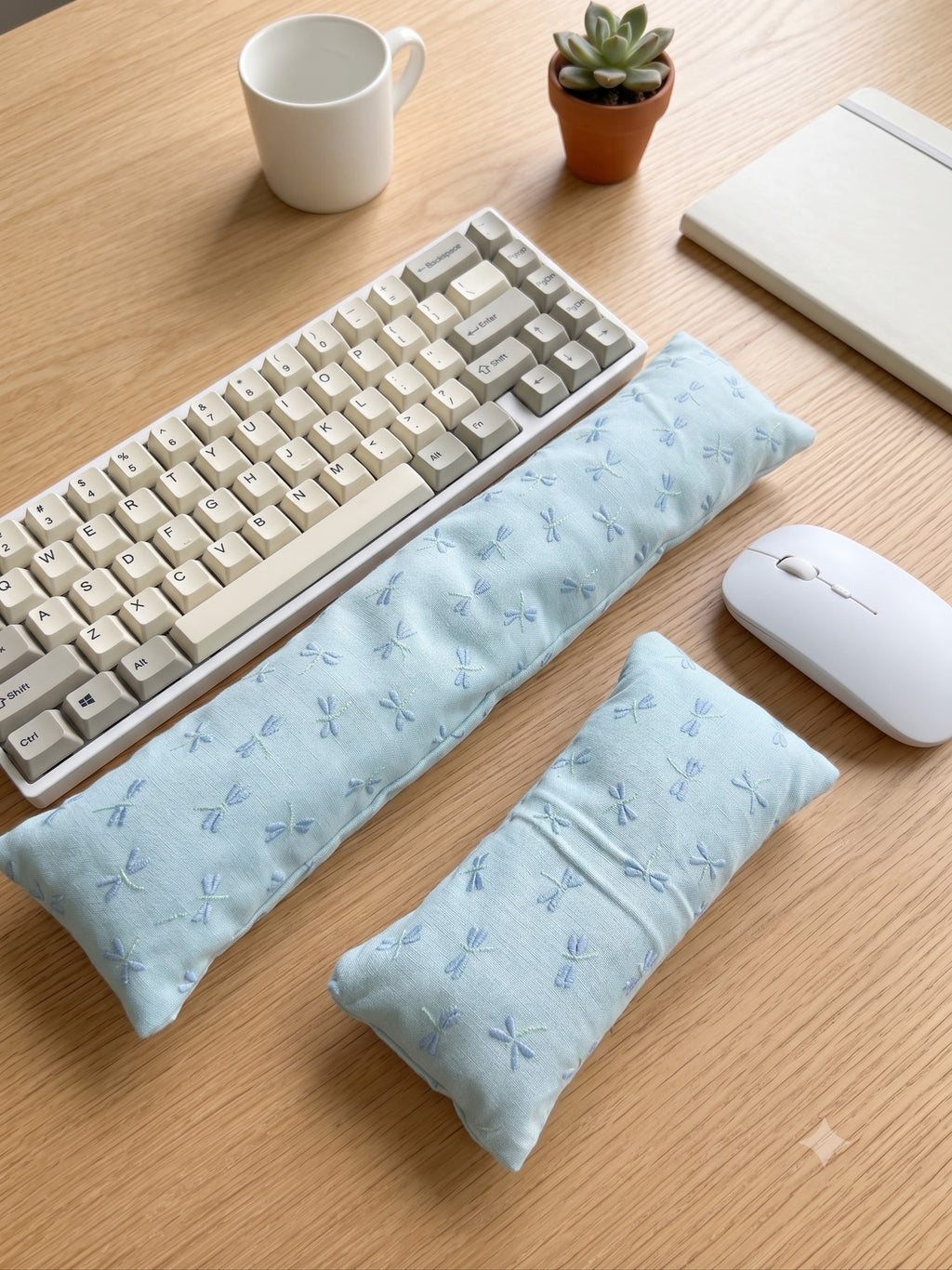 Embroidered dragonfly keyboard and mouse wrist rests beside a keyboard on a wooden desk