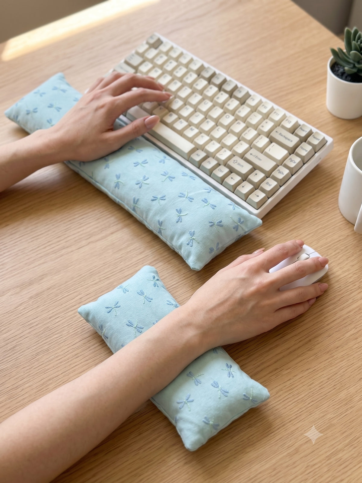 Hands on a keyboard and mouse resting on the embroidered dragonfly wrist rests