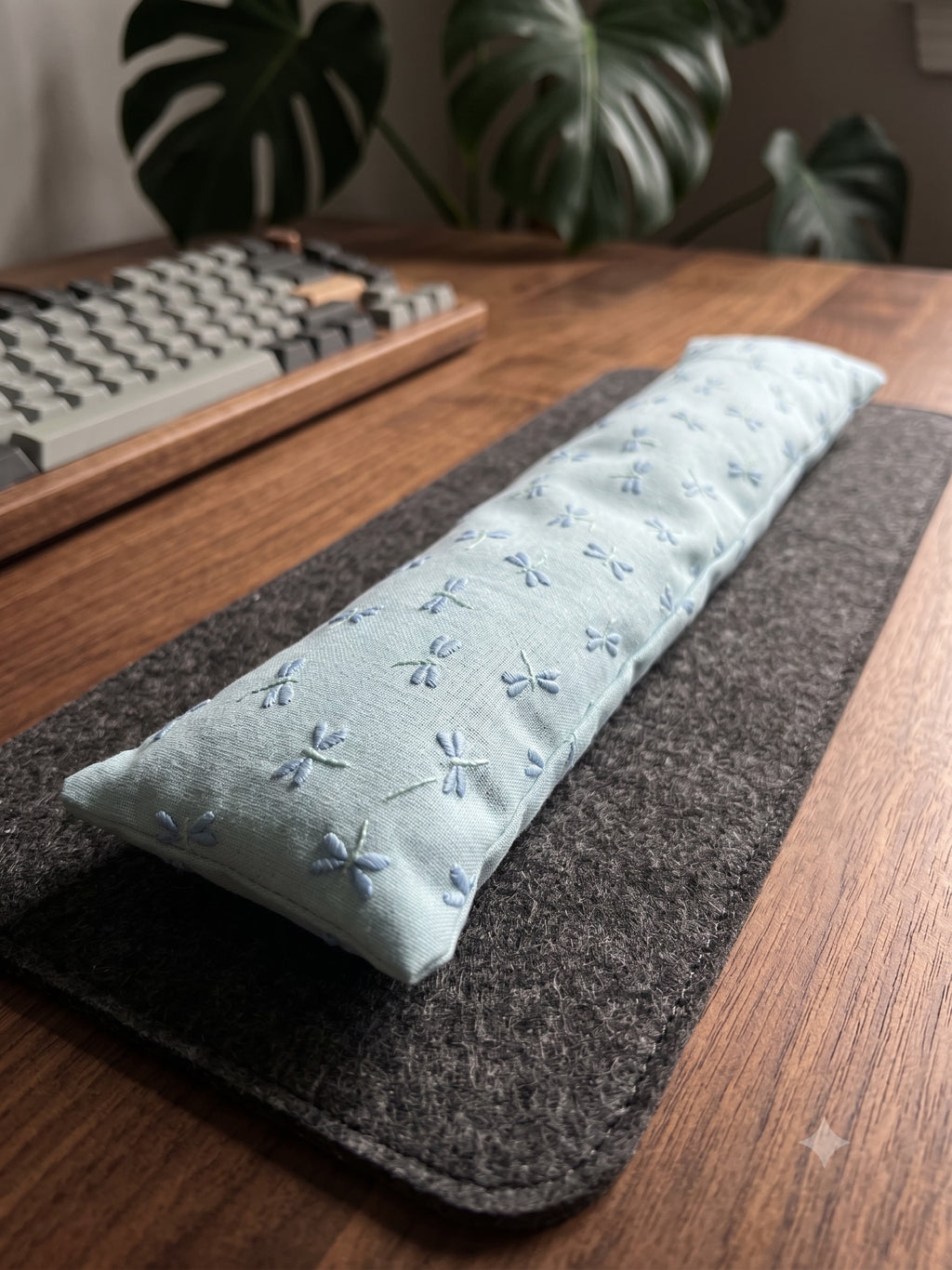 Embroidered dragonfly keyboard wrist rest on a felt desk mat in front of a wooden keyboard