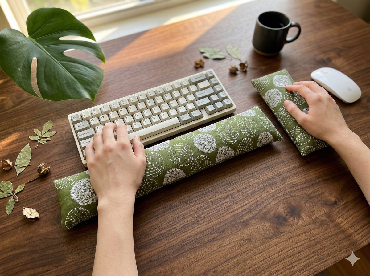 Hands typing on a keyboard above the olive green embroidered leaf wrist rest on a dark wood desk