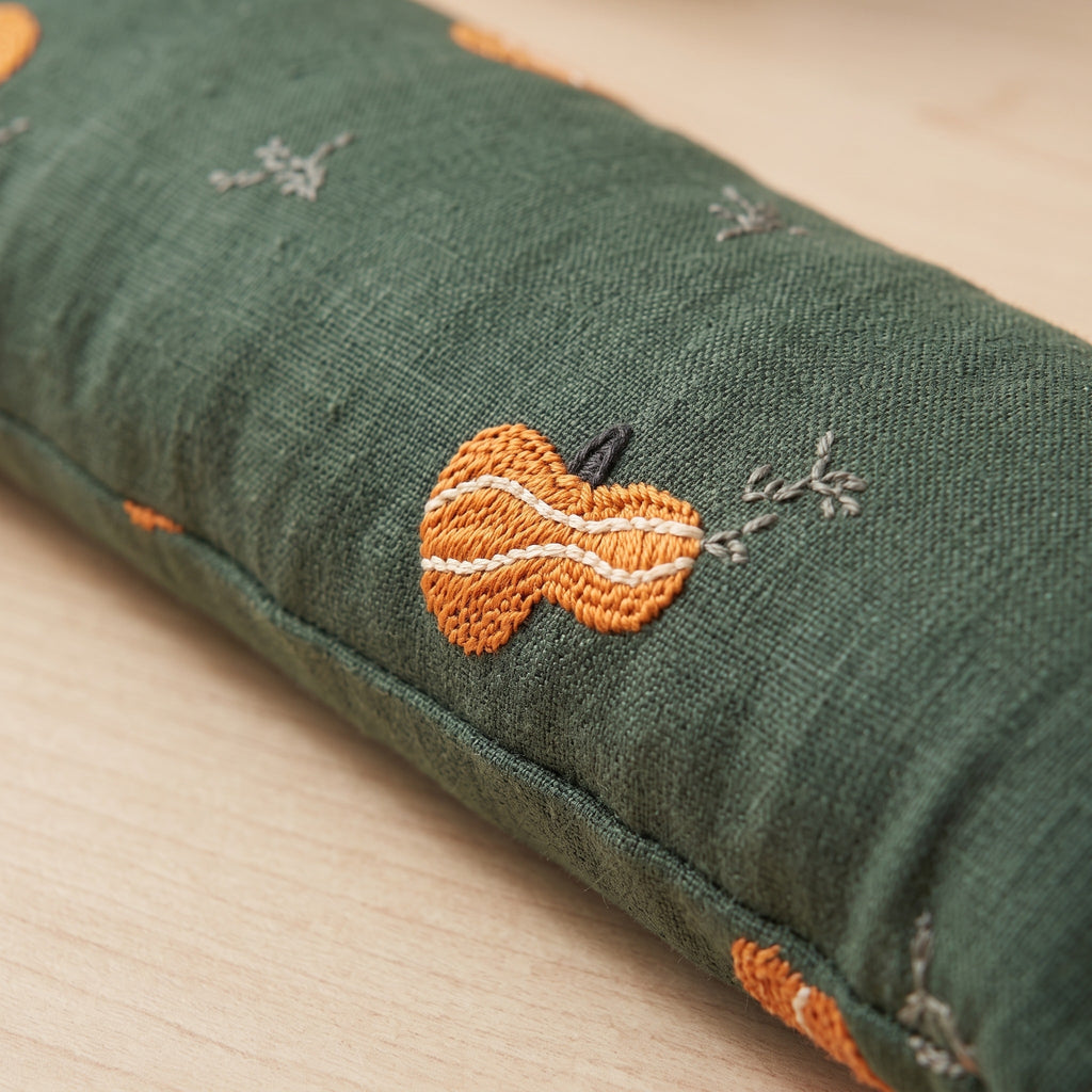Close-up of an orange pumpkin embroidered in textured thread on forest green fabric