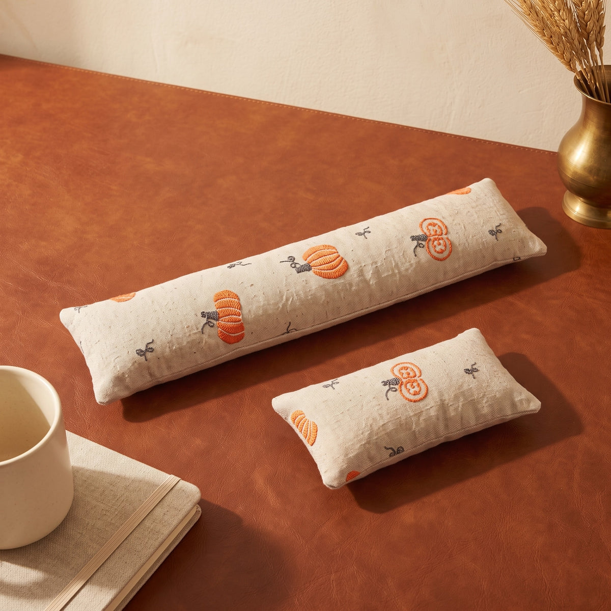 Cream embroidered pumpkin keyboard and mouse wrist rests on a rust leather desk mat