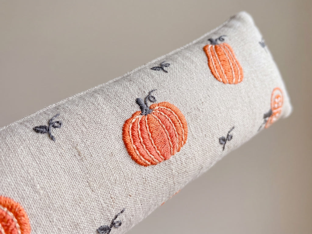 Close-up of embroidered orange pumpkins and small vines on natural cream fabric