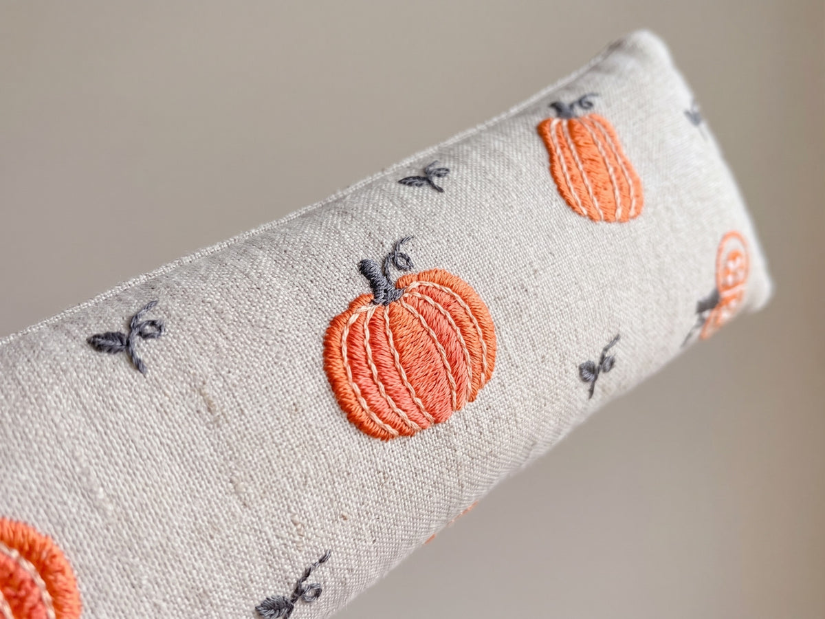Close-up of embroidered orange pumpkins and small vines on natural cream fabric