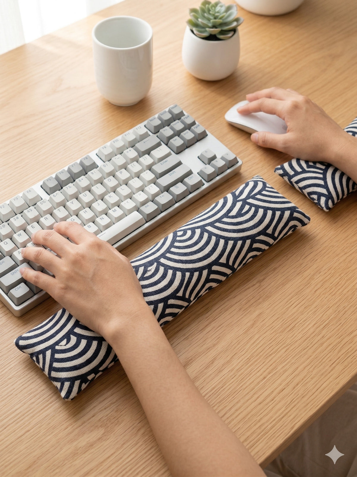 Hands on a keyboard and mouse resting on the navy and cream geometric arc wrist rests
