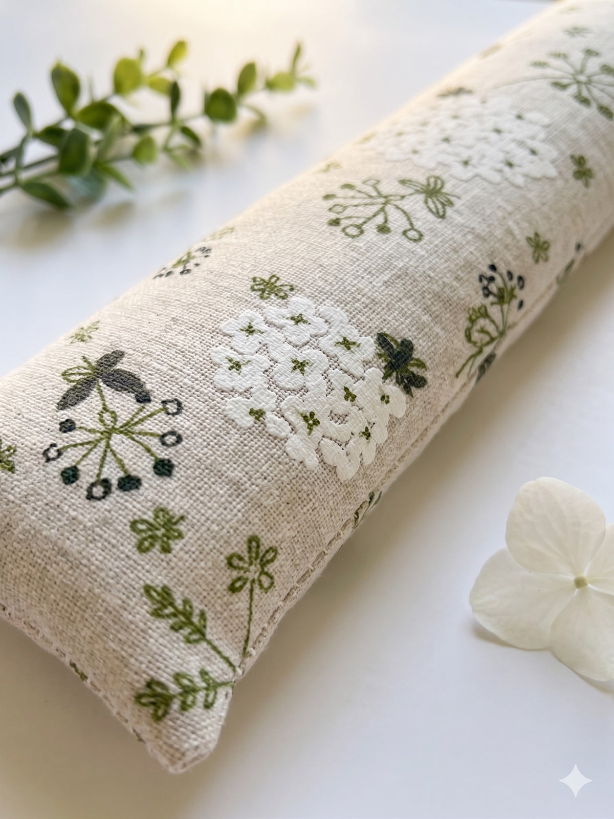 Close-up of white hydrangea and green botanical sprigs on natural fabric