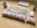Lilac floral corduroy keyboard and mouse wrist rests around a keyboard on a wooden desk