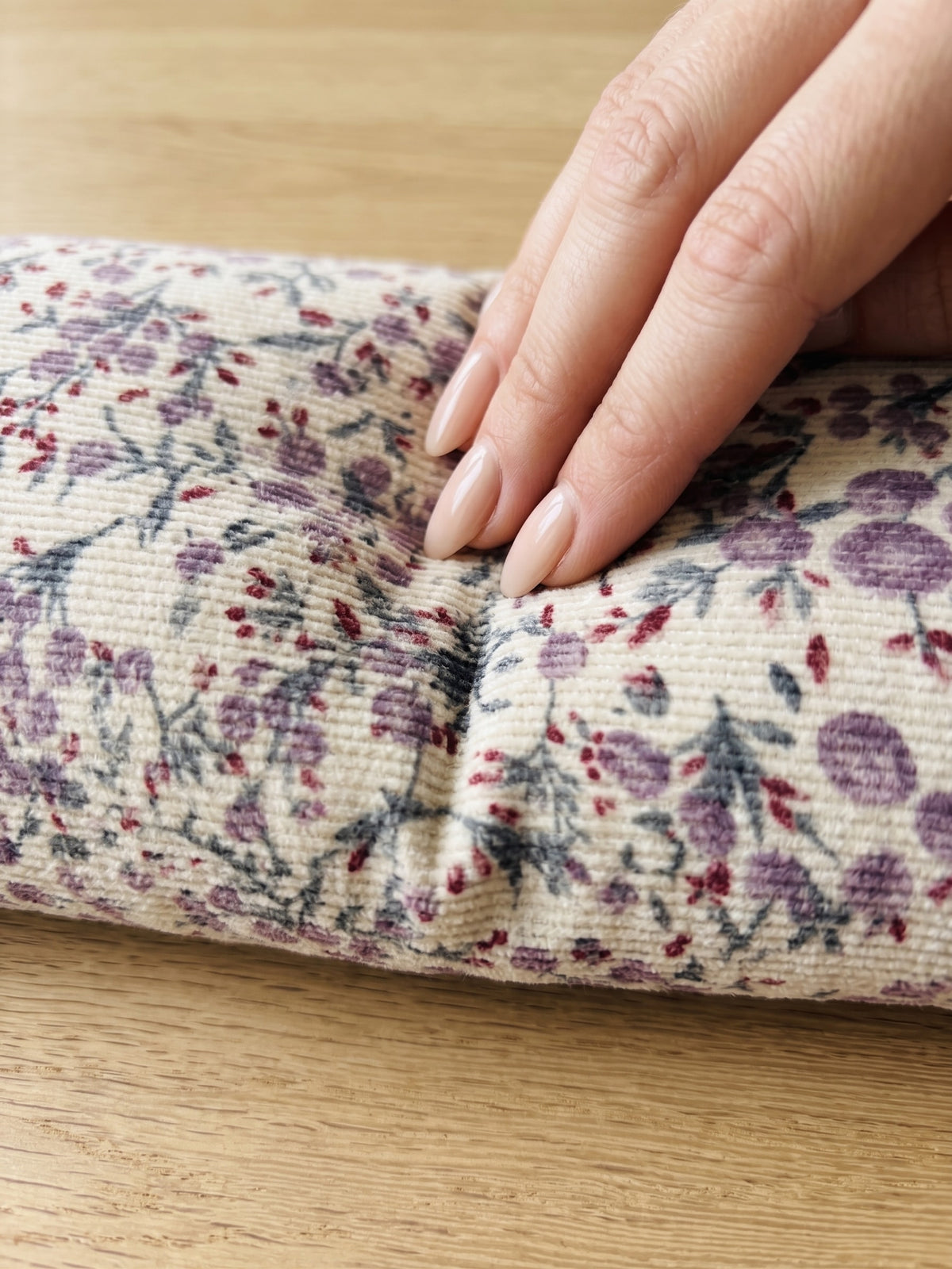 Fingers pressing into the lilac floral corduroy wrist rest to show the buckwheat filling