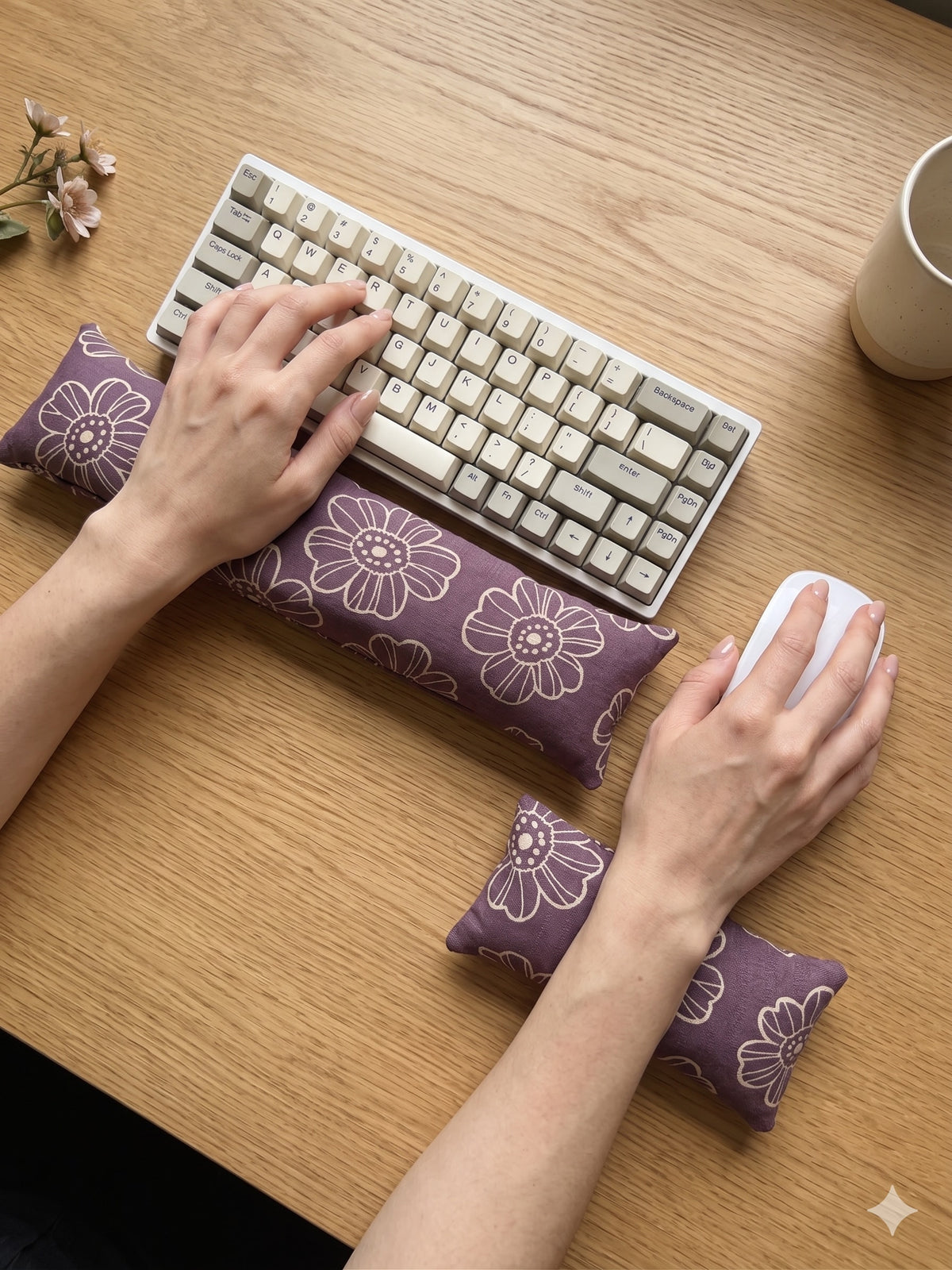Hands on a keyboard and mouse resting on the plum daisy wrist rests