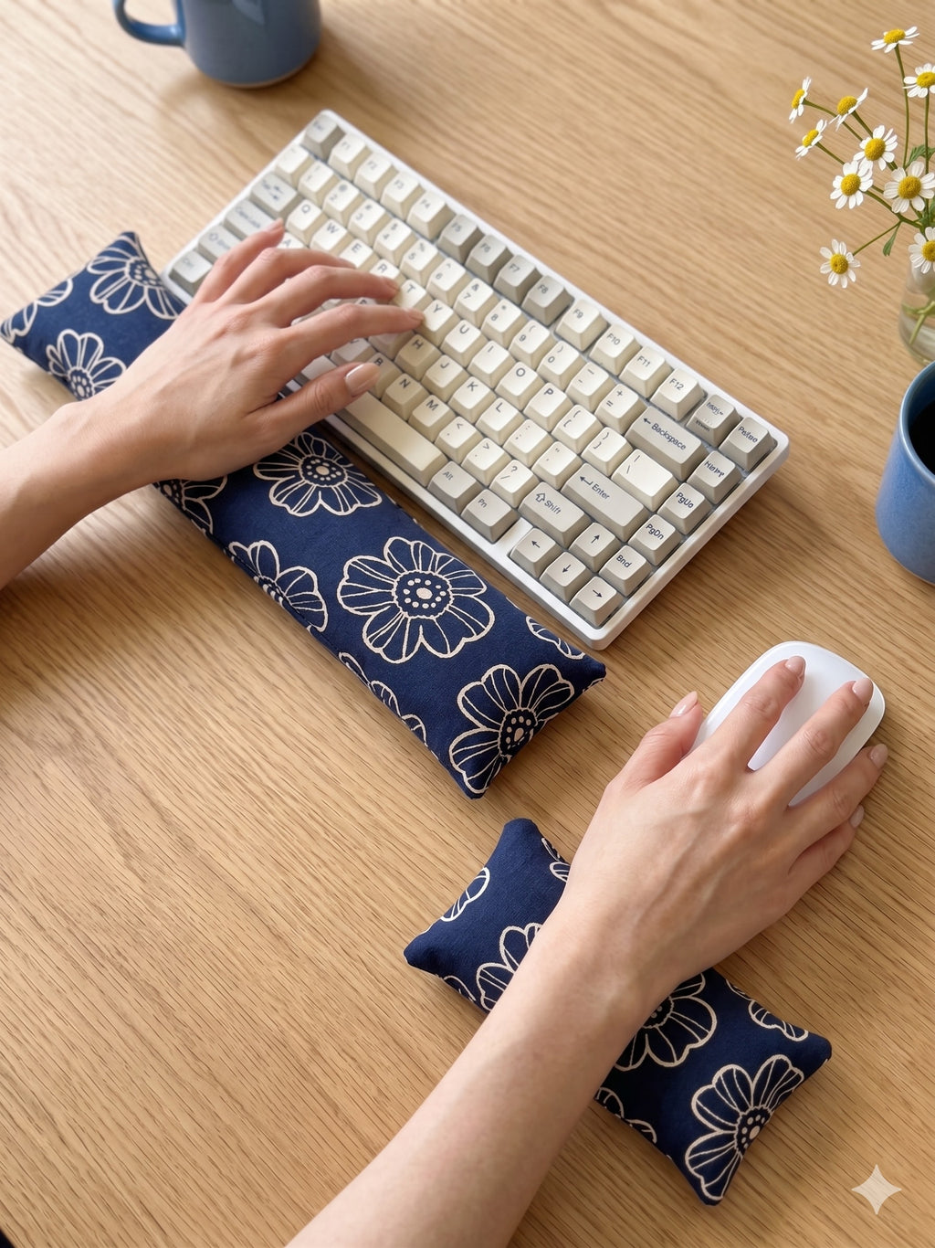 Hands on a keyboard and mouse resting on the navy daisy wrist rests