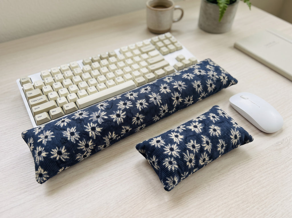 Navy daisy corduroy keyboard and mouse wrist rests beside a keyboard on a light wood desk