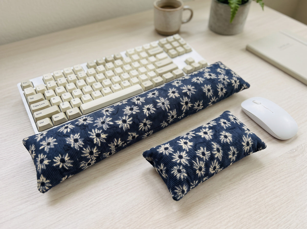 Navy daisy corduroy keyboard and mouse wrist rests beside a keyboard on a light wood desk