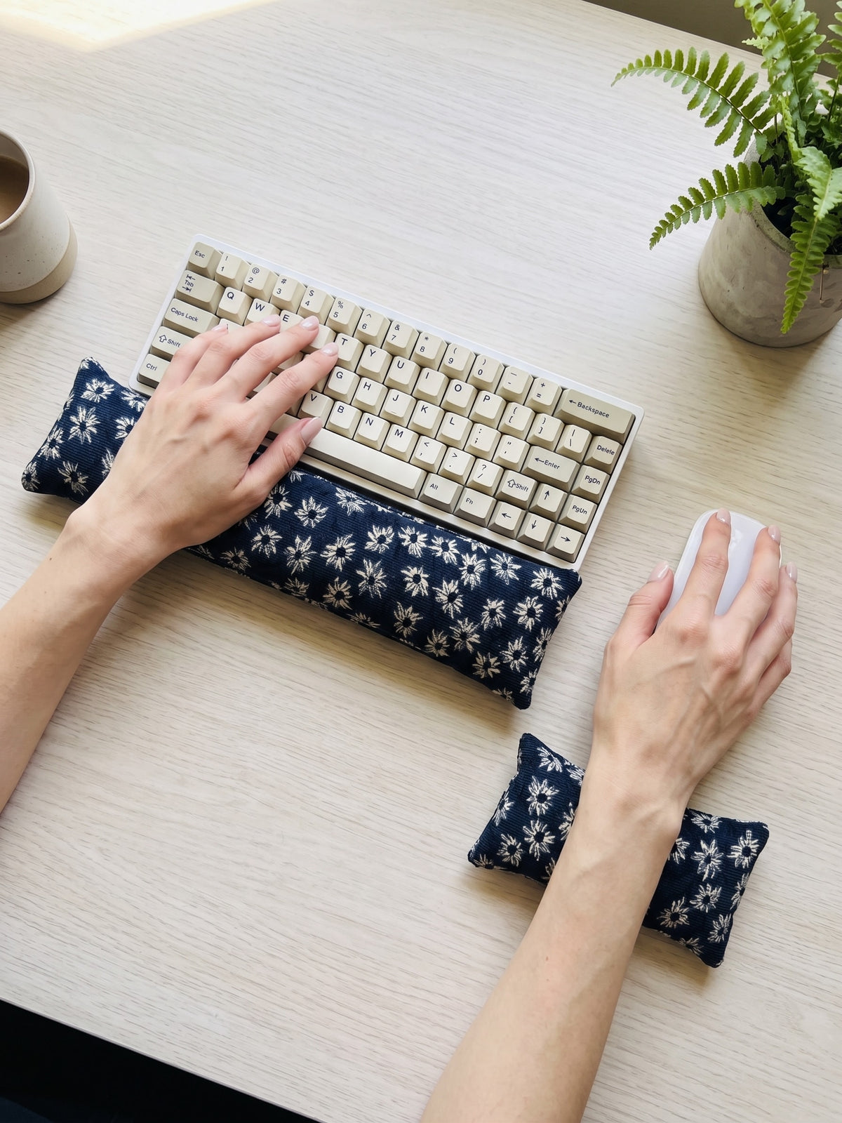 Hands on a keyboard and mouse resting on the navy daisy corduroy wrist rests