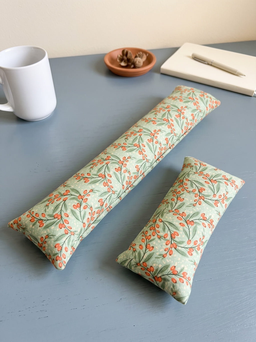The two pieces of the sage berry set, a keyboard wrist rest and a mouse wrist rest, with a mug