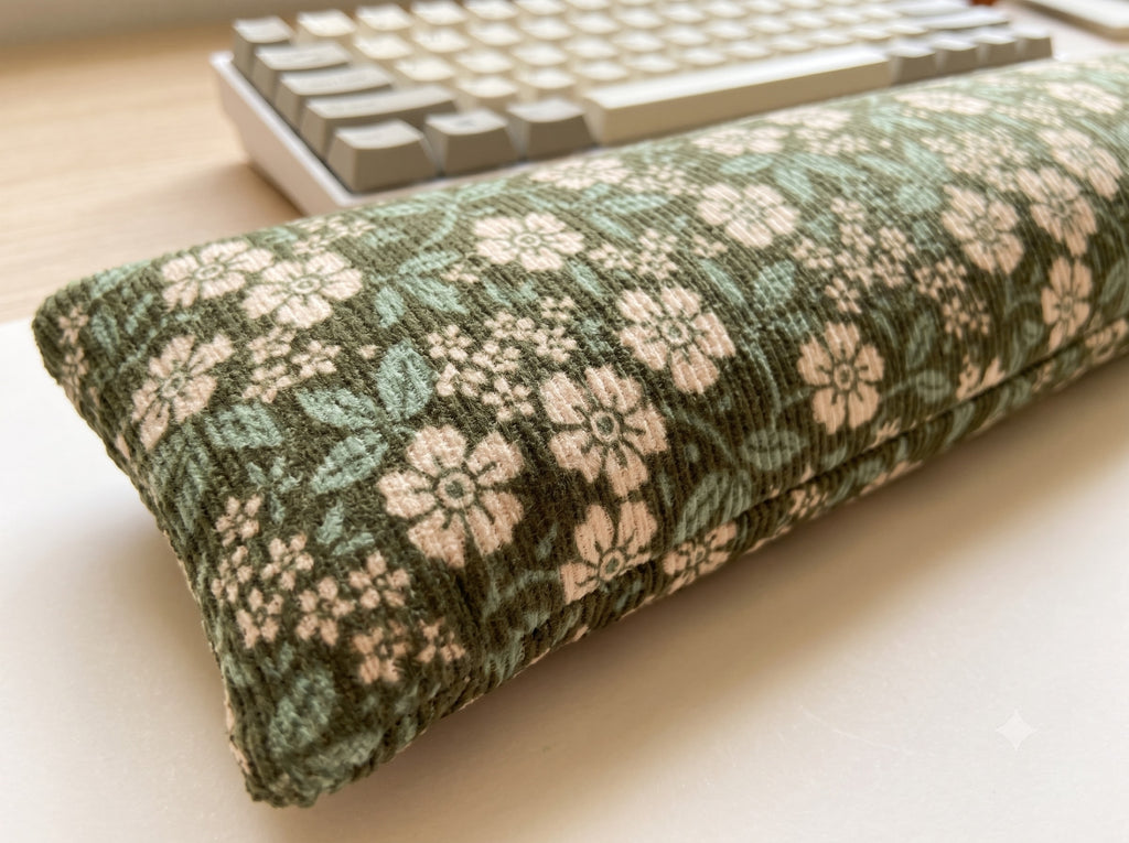 Close-up of cream blossoms and teal leaves on ribbed sage green corduroy