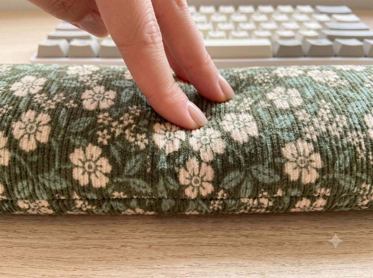 Fingers pressing into the sage floral corduroy wrist rest to show the buckwheat filling