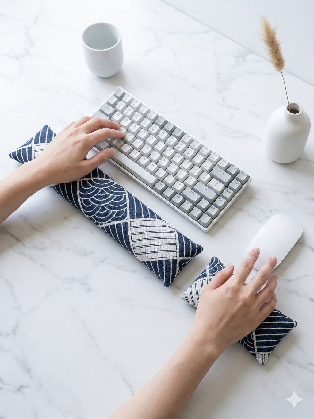 Hands on a keyboard and mouse resting on the sashiko boro wrist rests on a white marble desk