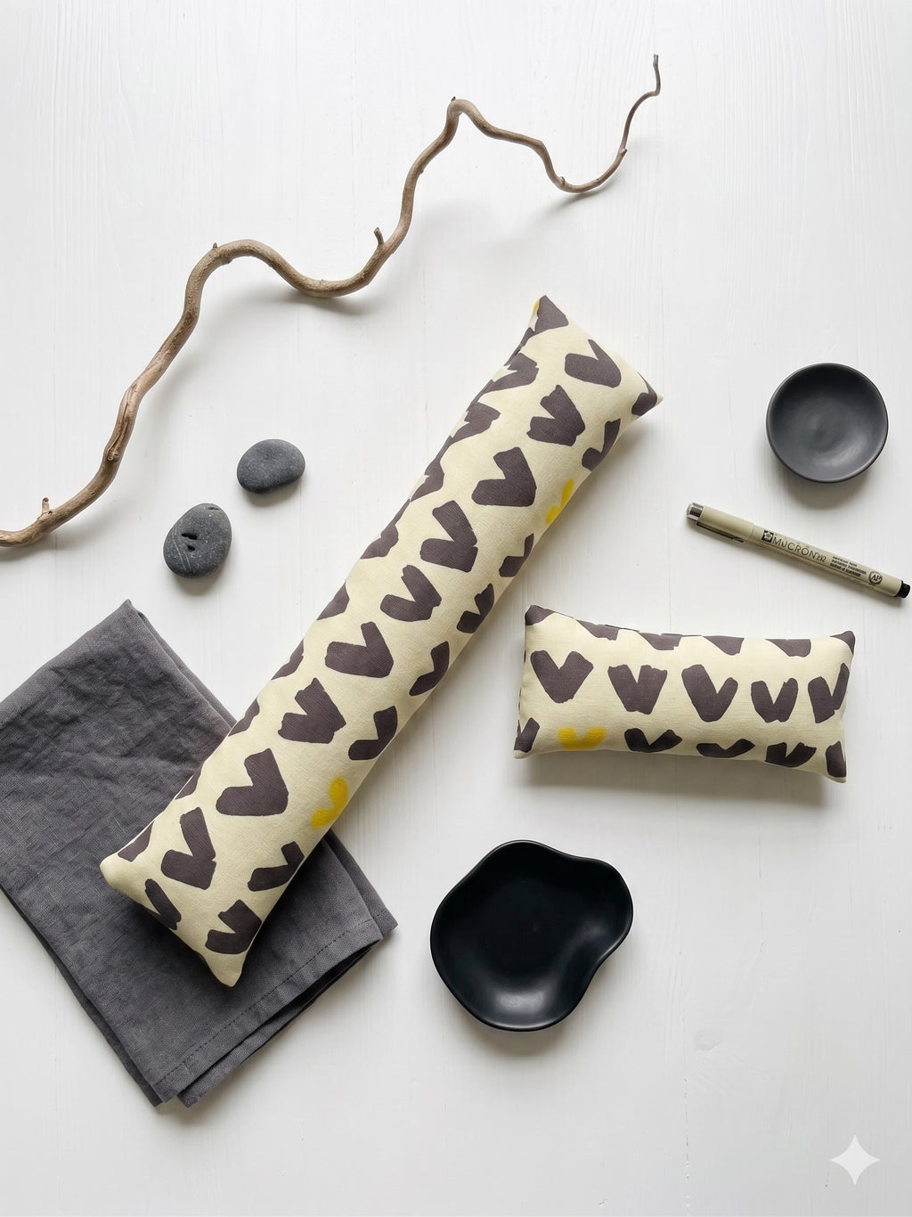 The two pieces of the scandi abstract set laid flat with dark stones and a branch