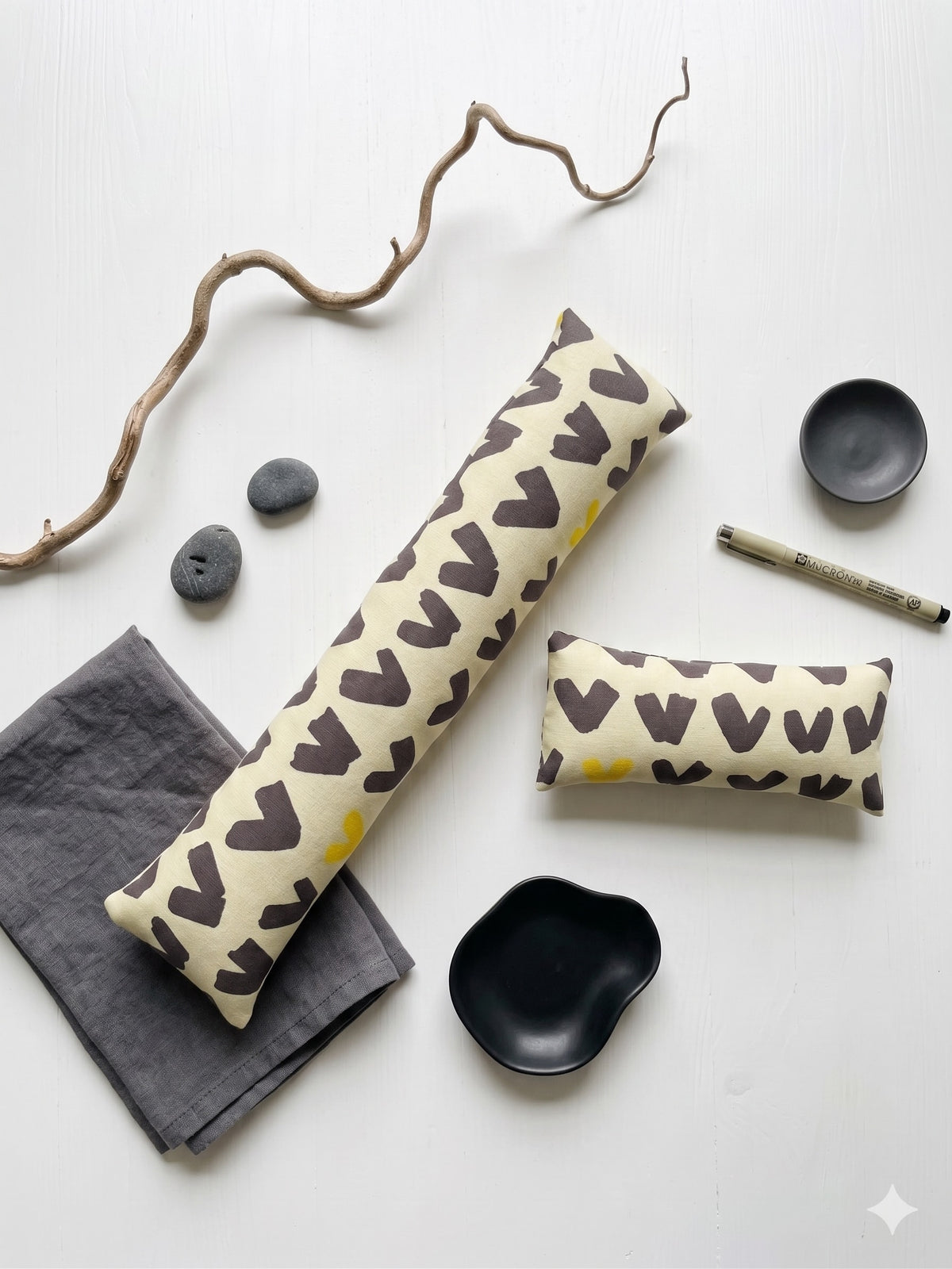 The two pieces of the scandi abstract set laid flat with dark stones and a branch