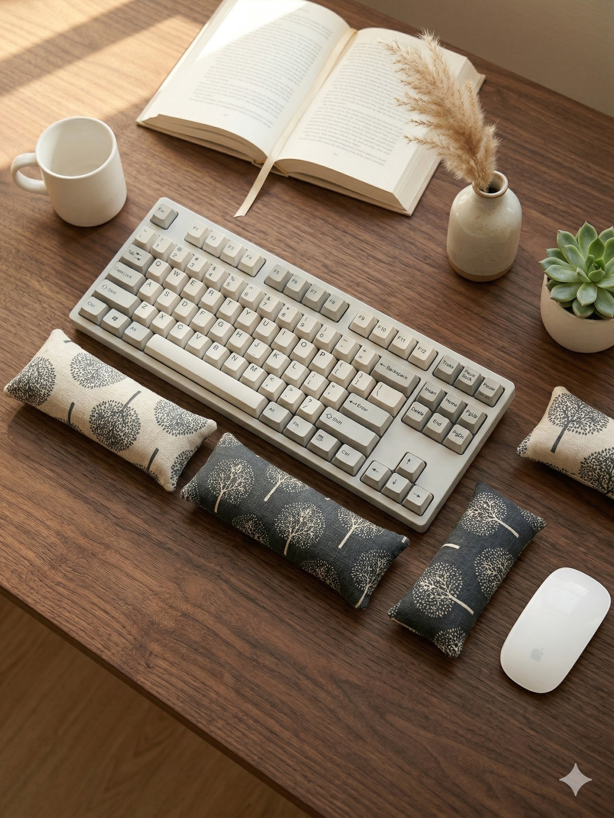 Tree print wrist rests around a keyboard on a dark wood desk with a mug and an open book
