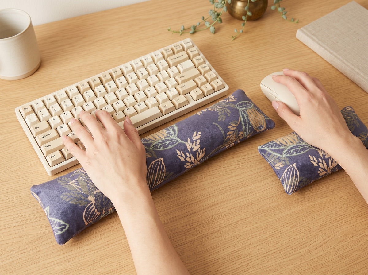 Hands on a keyboard and mouse resting on the dusky blue velvet wrist rests