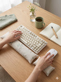 Hands on a keyboard and mouse resting on the wildflower sprig wrist rests on a wooden desk