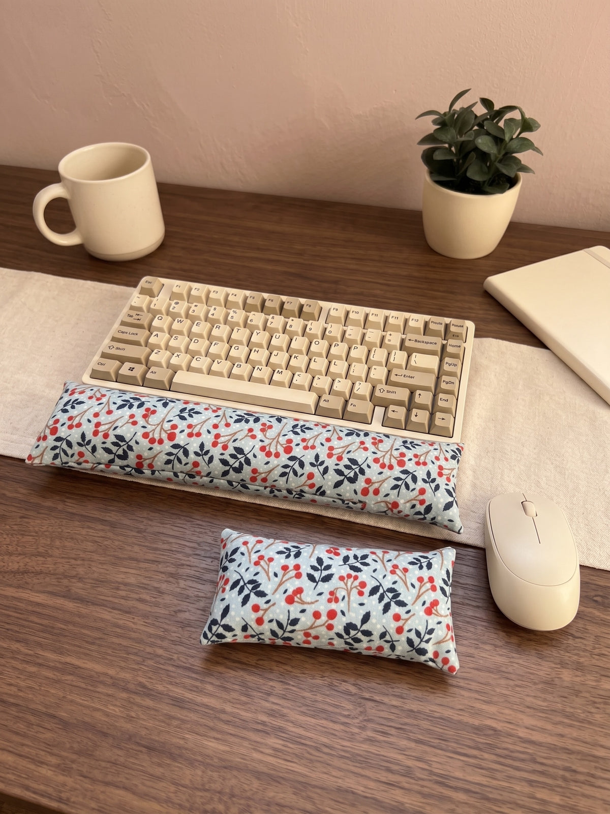 Winterberry keyboard and mouse wrist rests in front of a keyboard on a wooden desk with a mug and plant